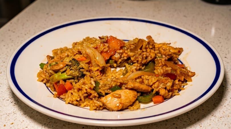 Chicken fried rice with broccoli, carrots, and onions on a white plate with a blue rim.